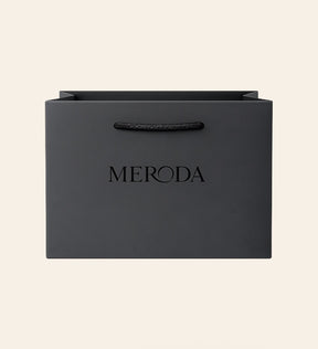 Mattschwarze Geschenktasche mit Kordelgriff und geprägtem Meroda Logo vor cremefarbenem Hintergrund.