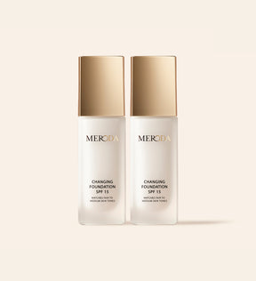 Zwei Meroda Changing Foundation Flakons mit goldenen Kappen nebeneinander auf neutralem Hintergrund.