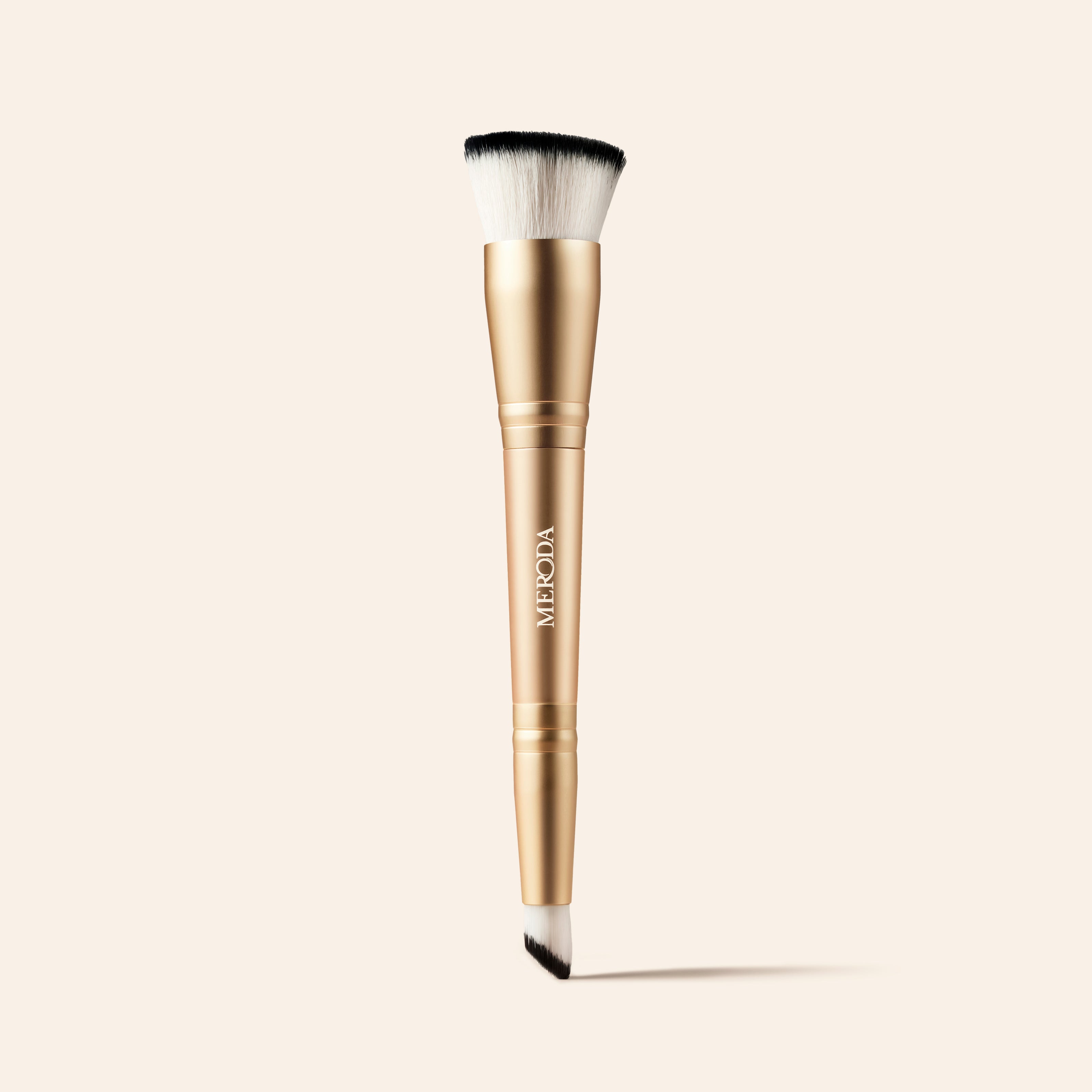 2-in-1 Build & Conceal Brush mit goldenem Griff und zweiseitigen Synthetikborsten auf neutralem Hintergrund.