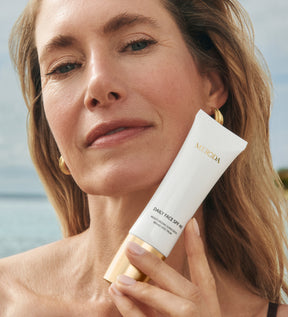 Daily Face SPF 40 Tube, von einem Model mit strahlender Haut vor einer sonnigen Strandkulisse präsentiert.