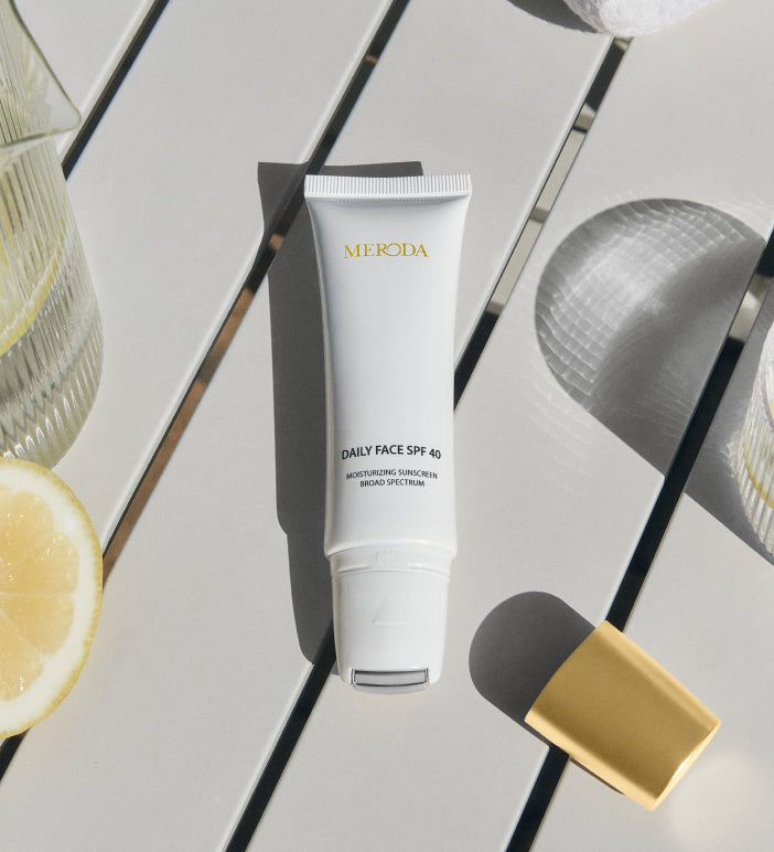 Daily Face SPF 40 Tube mit kühlendem Metall-Rollerball-Applikator auf hellem Tisch mit Zitronenscheibe.