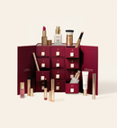 Festlicher dunkelroter Adventskalender mit nummerierten Schubladen, präsentiert mit verschiedenen Meroda Beauty-Produkten und einem Foundation-Pinsel.