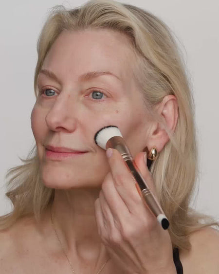 Reifere blonde Frau trägt Changing Foundation mit einem 2-in-1-Pinsel für ein ebenmässiges, natürliches Finish auf.